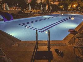 piscine à l'hôtel le soir. reste de touristes près de l'eau le soir. les affaires des gens se trouvent à proximité, les parapluies sont pliés sans soleil. eau bleue dans la piscine photo