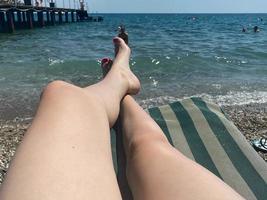 La section basse de la femme sur une chaise longue à la plage par mer contre un ciel clair photo