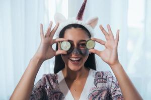 femme de spa souriante drôle avec un masque facial frais tenir des concombres. photo