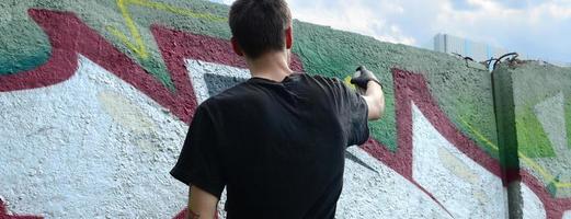 un jeune hooligan peint des graffitis sur un mur de béton. concept de vandalisme illégal. art de rue photo