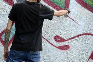 un jeune hooligan peint des graffitis sur un mur de béton. concept de vandalisme illégal. art de rue photo