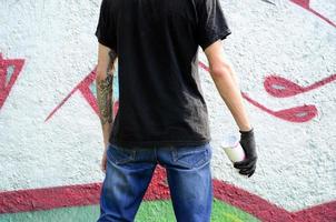 un jeune hooligan avec une bombe aérosol se dresse contre un mur de béton avec des graffitis. concept de vandalisme illégal. art de rue photo