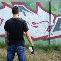 un jeune hooligan avec une bombe aérosol se dresse contre un mur de béton avec des graffitis. concept de vandalisme illégal. art de rue photo