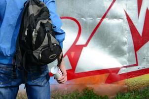 un jeune graffeur avec un sac noir regarde le mur avec son graffiti sur un mur. notion d'art de rue photo