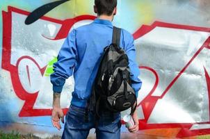 un jeune graffeur avec un sac noir regarde le mur avec son graffiti sur un mur. notion d'art de rue photo