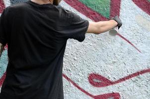 un jeune hooligan peint des graffitis sur un mur de béton. concept de vandalisme illégal. art de rue photo