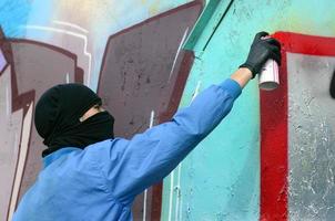 un jeune hooligan au visage caché peint des graffitis sur un mur métallique. concept de vandalisme illégal photo