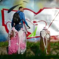 quelques pots de peinture usagés sur le fond de l'espace avec le mur sur lequel le jeune homme dessine un grand dessin graffiti. art moderne de dessiner des murs en graffiti photo