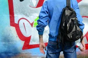 un jeune graffeur avec un sac noir regarde le mur avec son graffiti sur un mur. notion d'art de rue photo