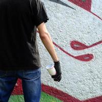 un jeune hooligan avec une bombe aérosol se dresse contre un mur de béton avec des graffitis. concept de vandalisme illégal. art de rue photo