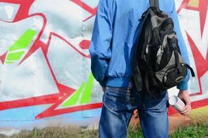 un jeune graffeur avec un sac noir regarde le mur avec son graffiti sur un mur. notion d'art de rue photo