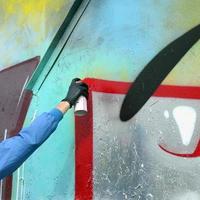 une main avec une bombe aérosol qui dessine un nouveau graffiti sur le mur. photo du processus de dessin d'un graffiti sur un mur métallique. le concept d'art de rue et de vandalisme illégal