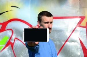 le graffeur montre un smartphone avec un écran noir vide sur fond de mur peint coloré. notion d'art de rue photo
