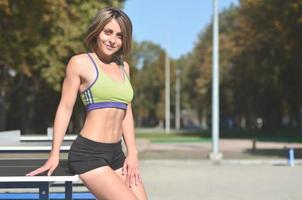 une jeune athlète caucasienne dans un vêtement de sport vert vif se tient près d'une table de ping-pong sur fond d'une salle de sport de rue. sports d'été et concept de mode de vie sain photo