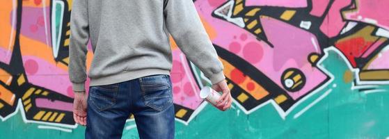 un jeune graffeur dans un sweat à capuche gris regarde le mur avec photo