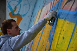 un jeune graffeur aux cheveux roux peint un nouveau graffiti sur le mur. photo du processus de dessin d'un graffiti sur un mur en gros plan. le concept d'art de rue et de vandalisme illégal