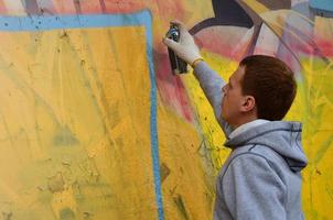 un jeune graffeur aux cheveux roux peint un nouveau graffiti sur le mur. photo du processus de dessin d'un graffiti sur un mur en gros plan. le concept d'art de rue et de vandalisme illégal