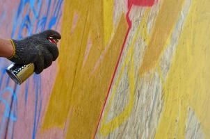 une main avec une bombe aérosol qui dessine un nouveau graffiti sur le mur. photo du processus de dessin d'un graffiti sur un gros plan de mur en bois. le concept d'art de rue et de vandalisme illégal