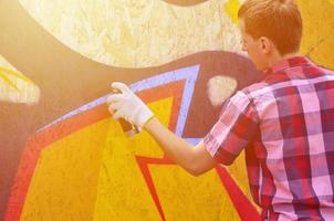 un jeune graffeur aux cheveux roux peint un nouveau graffiti sur le mur. photo du processus de dessin d'un graffiti sur un mur en gros plan. le concept d'art de rue et de vandalisme illégal