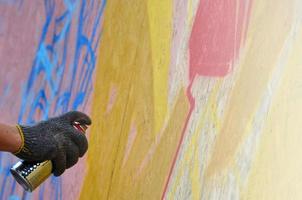 une main avec une bombe aérosol qui dessine un nouveau graffiti sur le mur. photo du processus de dessin d'un graffiti sur un gros plan de mur en bois. le concept d'art de rue et de vandalisme illégal