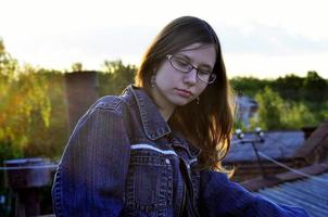 fille à lunettes et veste en jean repose sur le toit d'une maison photo