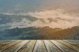 plancher de bois au premier plan sur le paysage du lever du soleil avec montagne et brouillard brouillard hiver météo éclairage solaire sous un ciel matinal coloré et vibrant dans les montagnes. nature montagne ciel et nuages coucher de soleil concept. photo