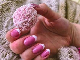 une fille avec une manucure française à la mode tient dans ses mains un bonbon rond en copeaux de noix de coco. joli dessert rose. bonbons à la noix de coco photo