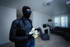 un voleur vêtu d'un sweat à capuche noir se tient avec un visage déguisé et tient beaucoup d'argent dans ses mains, a volé une grande quantité, un voleur a volé une télévision photo