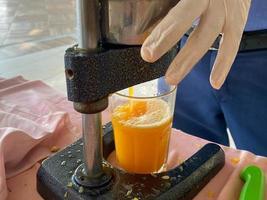 le processus de fabrication de jus d'orange jaune fraîchement pressé, un homme presse le jus dans un verre avec ses mains dans un hôtel dans un pays tropical chaud de l'est du paradis du sud photo