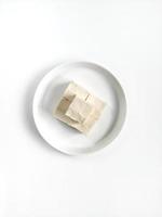 tofu blanc et lisse coupé en petits morceaux placés sur une plaque en céramique blanche isolée sur fond blanc. vue de dessus photo