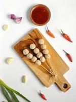 boulettes de viande en brochette avec sauce épicée sur la planche à découper en bois garnie d'ails, d'échalotes, de piments rouges et de poireaux photo