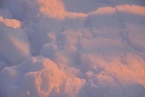 la neige rose hiverne à la lumière du soleil couchant. neige pelucheuse d'hiver rose et bleu en hiver. une congère dans les rayons du soleil couchant. photo