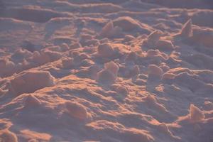 la neige rose hiverne à la lumière du soleil couchant. neige pelucheuse d'hiver rose et bleu en hiver. une congère dans les rayons du soleil couchant. photo