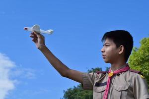 le scout asiatique tient un modèle d'avion blanc sur fond nuageux et bleu ciel, mise au point douce et sélective. photo