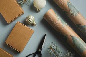 fond de noël avec coffrets cadeaux artisanaux, branches de sapin, papier d'emballage et décorations sur fond bleu. mise à plat photo