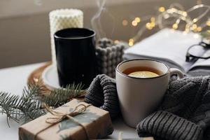 concept confortable de maison d'hiver. mug avec thé au citron, livre ouvert, pull chaud, bougies et sapin. bien-être, concept relaxant