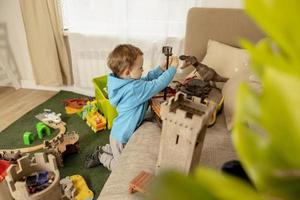 petit garçon caucasien avec sweat à capuche bleu jouant avec des jouets colorés à la maison. enfant s'amusant. un enfant heureux et joyeux joue avec un bateau, des dinosaures, un château. loisirs, vie domestique. chambre confortable. photo