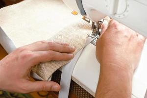 mains masculines cousant du tissu blanc sur une machine à coudre moderne. vue rapprochée du processus de couture. photo