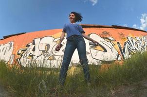 portrait d'une jeune fille émotionnelle aux cheveux noirs et aux piercings. une photo grand angle d'une fille avec des pots de peinture aérosol dans les mains sur un fond de mur de graffitis. un portrait moderne d'un objectif fisheye