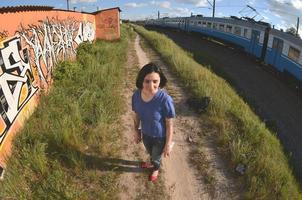 portrait d'une jeune fille émotionnelle aux cheveux noirs et aux piercings. une photo grand angle d'une fille avec des pots de peinture aérosol dans les mains sur un fond de mur de graffitis. un portrait moderne d'un objectif fisheye