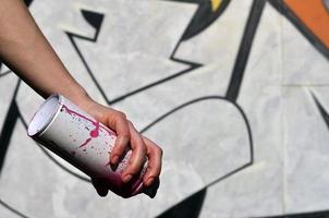 photo de la main d'une fille avec des pots de peinture aérosol dans les mains sur un fond de mur de graffiti. le concept d'art de rue et l'utilisation de peintures en aérosol. image d'arrière-plan de la boutique d'art graffiti