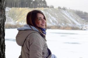 une jeune fille de race blanche dans un manteau marron est assise près d'une falaise à l'arrière-plan d'une ligne d'horizon entre le ciel et un lac gelé en hiver photo