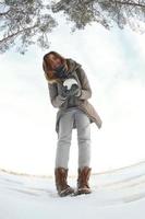 une jeune et joyeuse fille caucasienne en manteau marron tient une boule de neige devant une ligne d'horizon entre le ciel et un lac gelé en hiver. photo fisheye