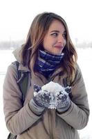 une jeune et joyeuse fille caucasienne dans un manteau marron tient une boule de neige à l'arrière-plan d'une ligne d'horizon entre le ciel et un lac gelé en hiver photo