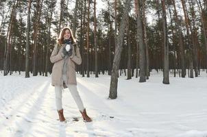 une jeune et joyeuse fille caucasienne en manteau marron tient une boule de neige dans une forêt enneigée en hiver. photo fisheye