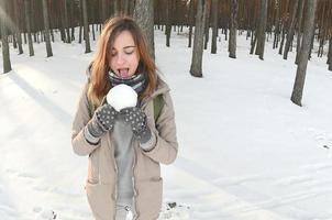 une jeune et joyeuse fille caucasienne en manteau marron tient une boule de neige dans une forêt enneigée en hiver. photo fisheye