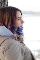 une jeune fille de race blanche dans un manteau marron regardant au loin sur la ligne d'horizon entre le ciel et le lac gelé en hiver photo