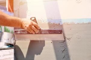 mains d'un vieux travailleur manuel avec des outils de plâtrage de mur rénovant la maison. plâtrier rénovant les murs extérieurs et les coins avec spatule et plâtre. isolation des murs. travaux de finition du bâtiment photo