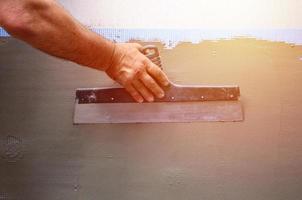 mains d'un vieux travailleur manuel avec des outils de plâtrage de mur rénovant la maison. plâtrier rénovant les murs extérieurs et les coins avec spatule et plâtre. isolation des murs. travaux de finition du bâtiment photo