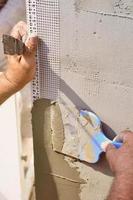 mains d'un vieux travailleur manuel avec des outils de plâtrage de mur rénovant la maison. plâtrier rénovant les murs extérieurs et les coins avec spatule et plâtre. isolation des murs. travaux de finition du bâtiment photo